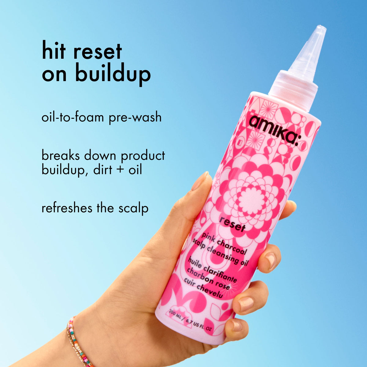 Pink bottle of Amika product held by a hand against a blue background