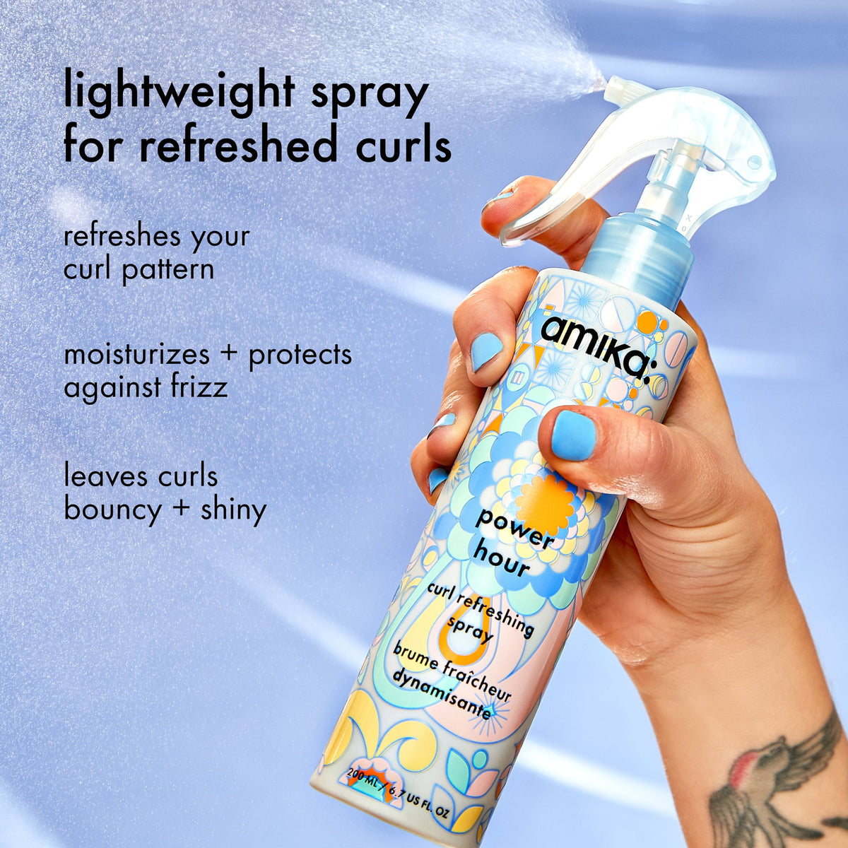 Amika power hour curl refreshing spray held by a hand with blue nail polish against a ligh