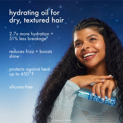 Woman with long, textured hair holding a bottle of hydrating oil against a blue background