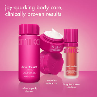 Three bright pink Amika body products are arranged on a pink surface, including a body was