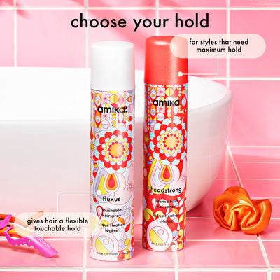 Two hair spray bottles with colorful designs on a pink tiled background.