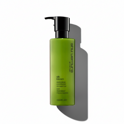 Green bottle of Shu Uemura Silk Bloom conditioner on a white background